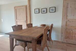 Una taula de dinar de fusta, caires de vimet, una porta de fusta i tres quadres penjats a la paret.