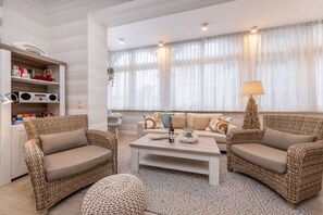Ein modernes Wohnzimmer mit Korbmöbeln, einem weißen Couchtisch und einem Bücherregal mit verschiedenen Gegenständen.