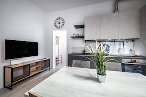 Una cuina moderna amb forn integrat, una zona de menjador amb taula gran i un televisor sobre un suport de fusta.