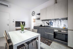 Eine moderne Küche mit grauen Schränken, einem eingebauten Backofen und einem Essbereich mit weißem Tisch und Stühlen.