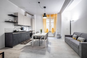 Una cuina moderna amb zona de menjador, un sofà gris i una finestra amb cortines grogues.
