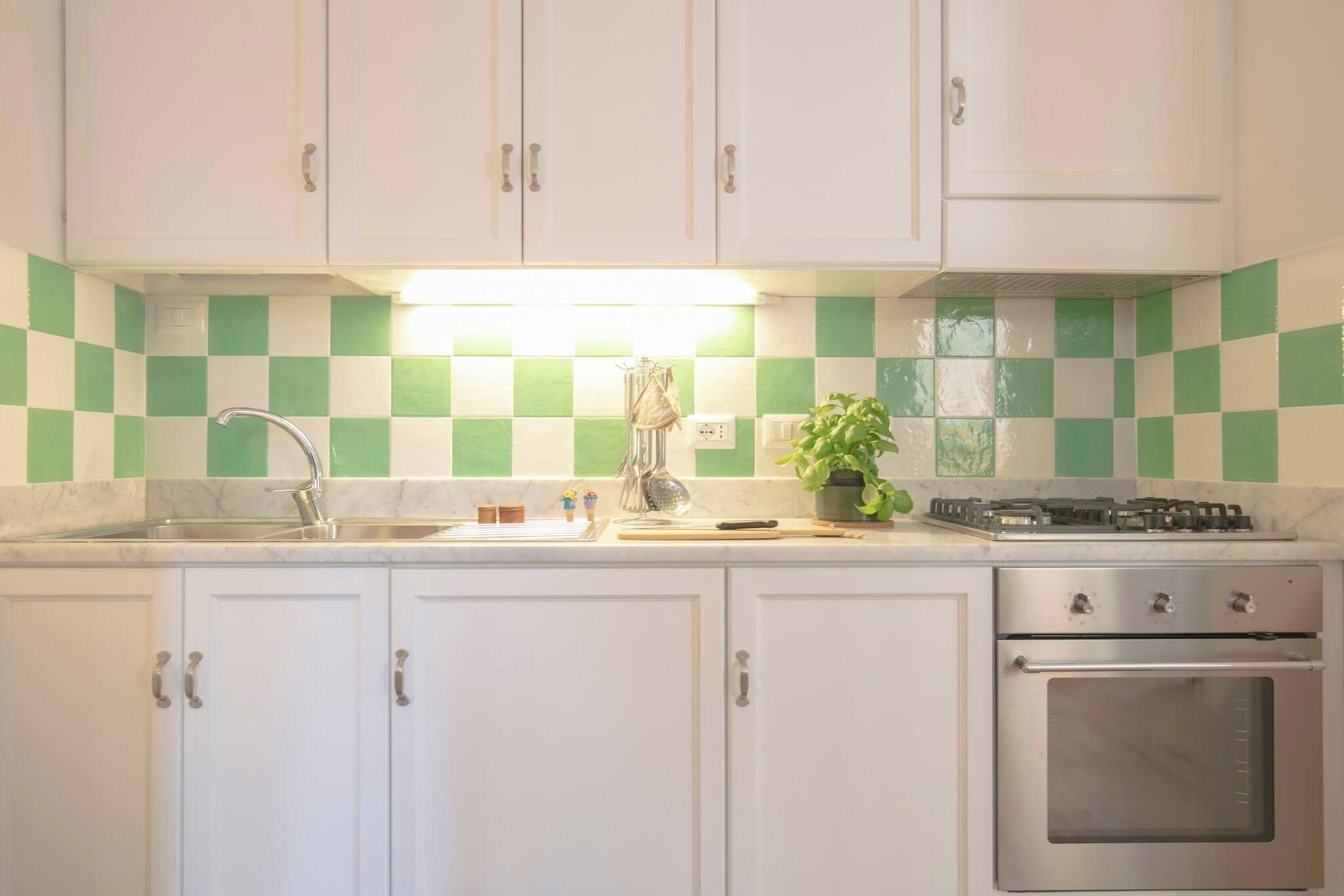 A kitchen with white cabinets, a sink, a stove, and a tiled backsplash.