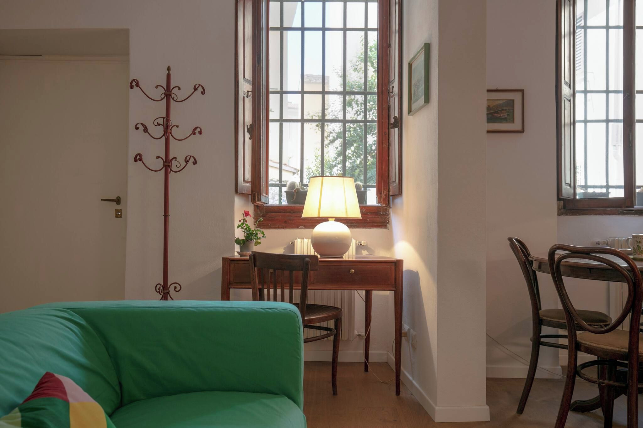A room with a green sofa, a wooden desk with a lamp, a chair, and a radiator.