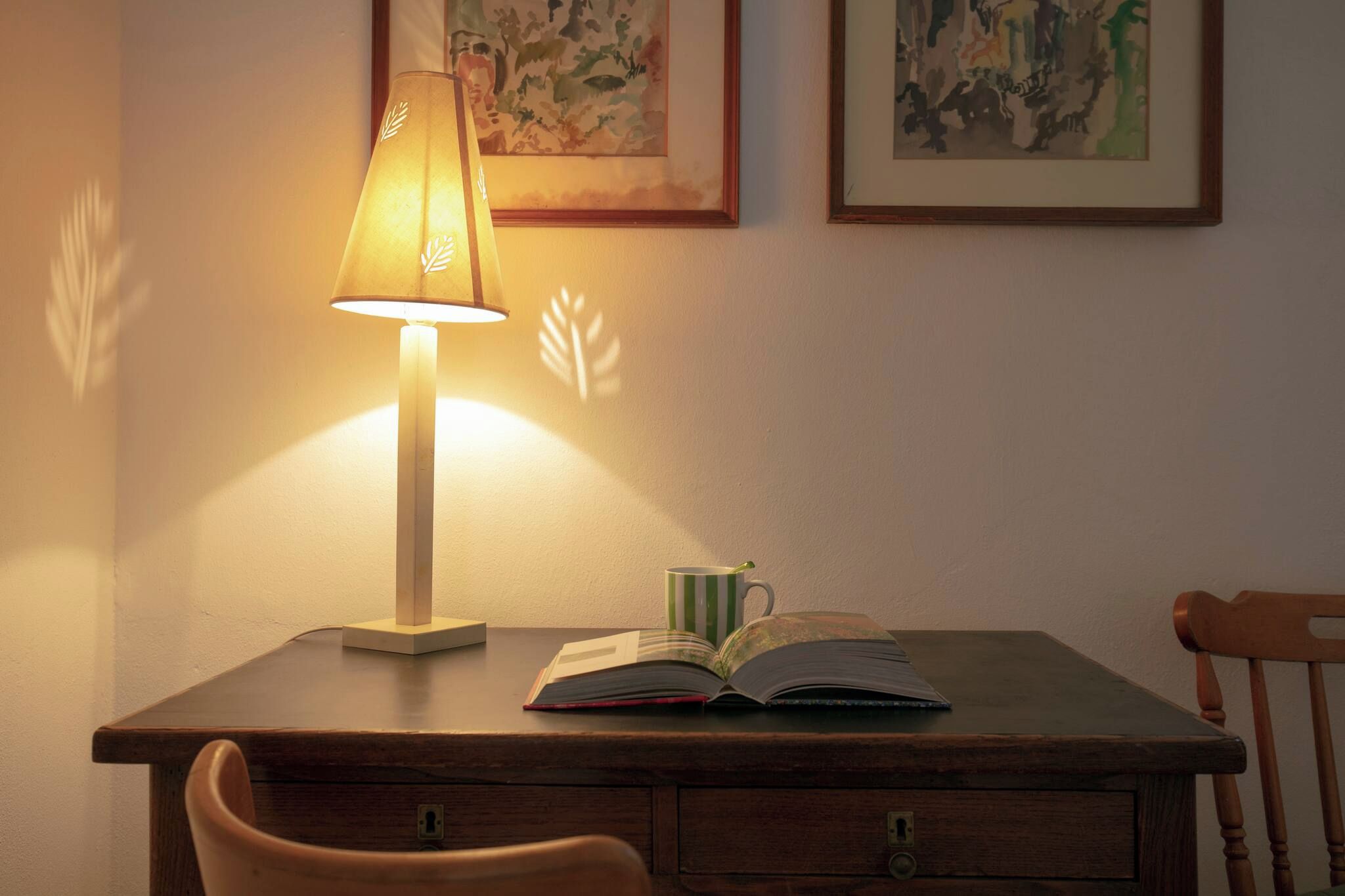 A wooden desk with a lamp, an open book, and a striped mug.