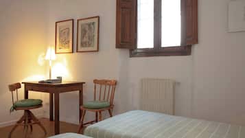 A room with a wooden desk, two chairs, a radiator, and two beds.