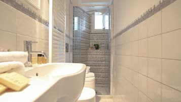 Ein schmales Badezimmer mit einem weißen Waschbecken, einer Toilette und einer Duschkabine mit Glastür.