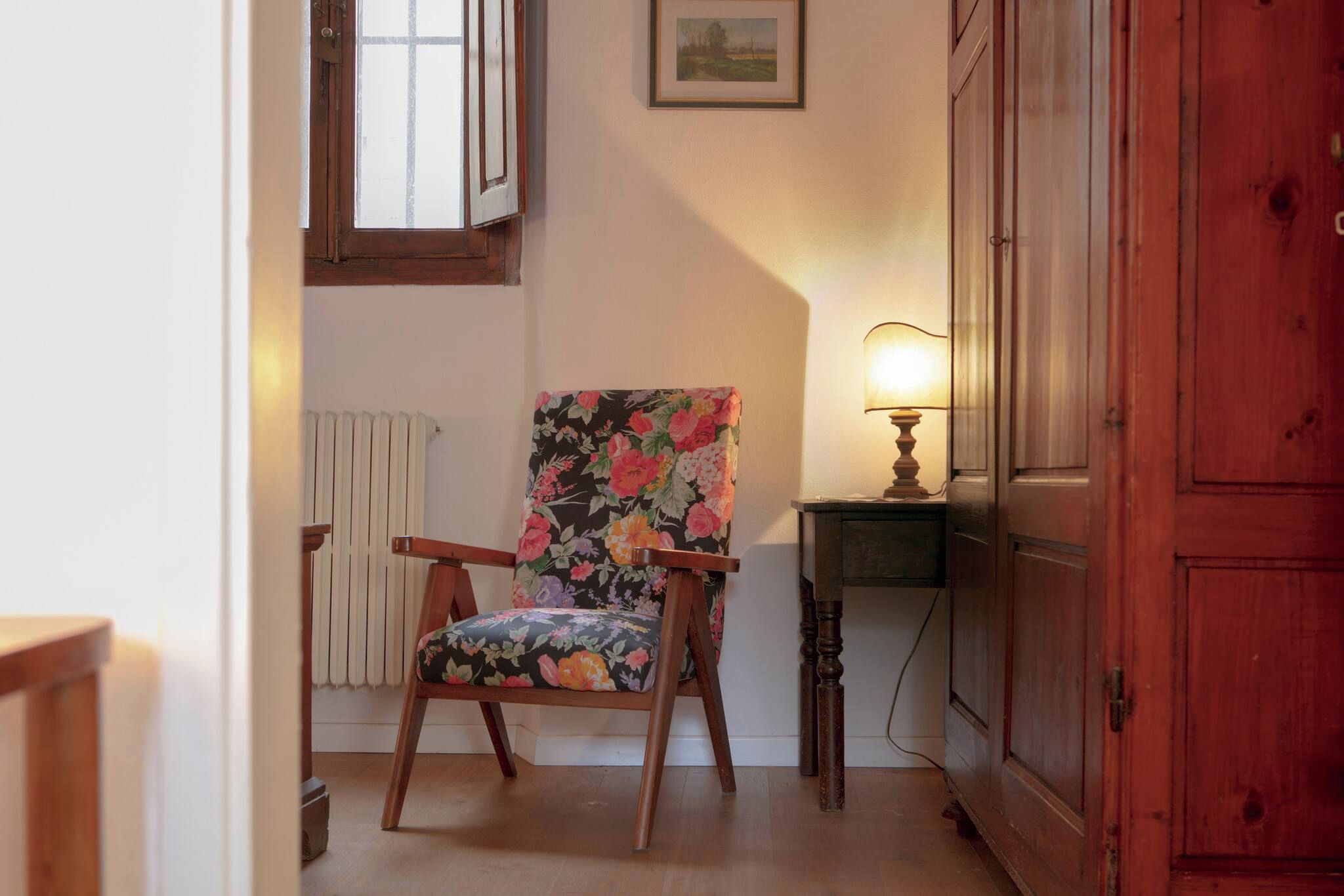 A chair with floral upholstery, a wooden cabinet, and a table with a lamp.