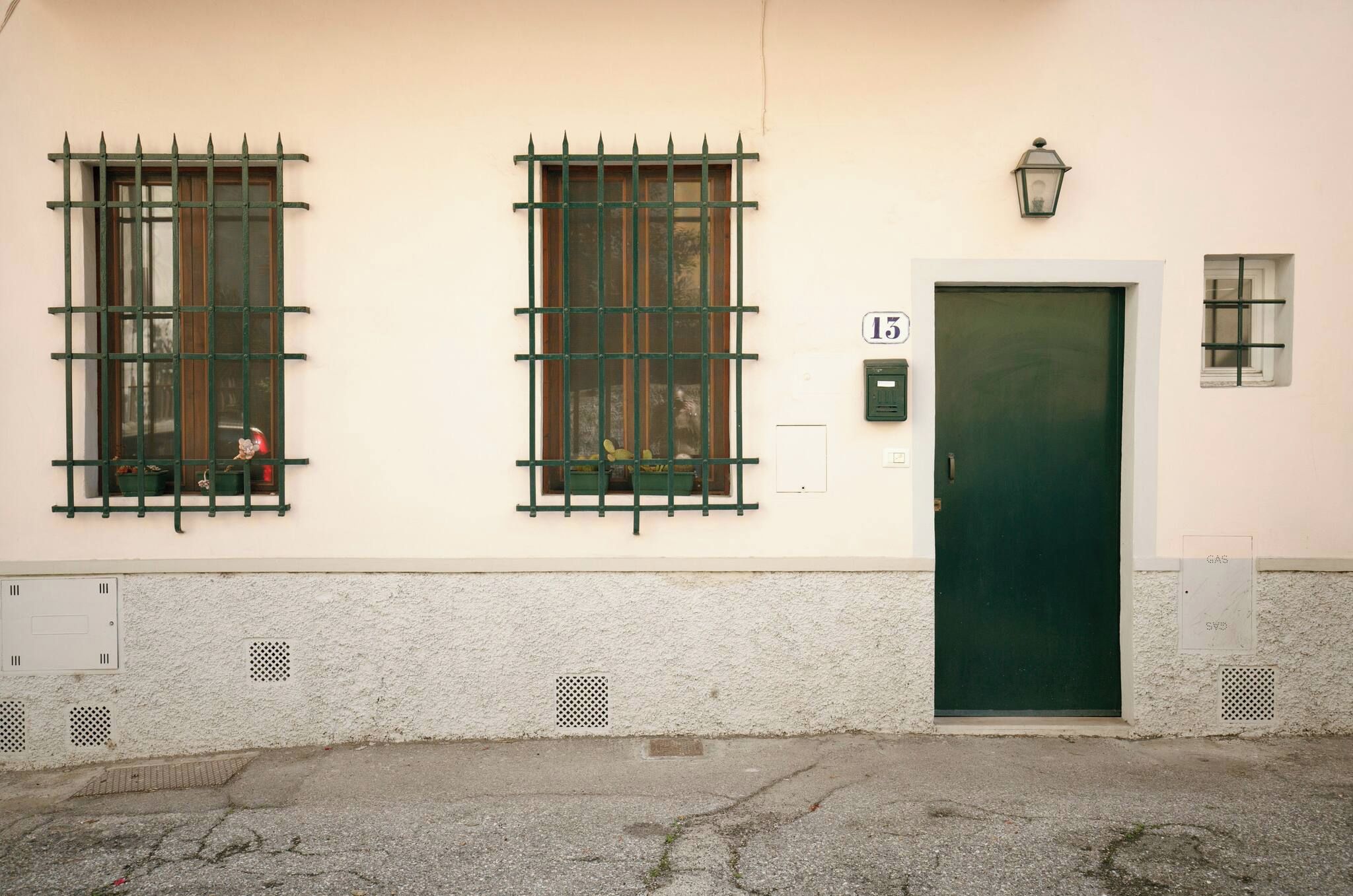 Un edificio con dos ventanas de celosía metálica, una puerta verde y un ventanal con una reja de metal.