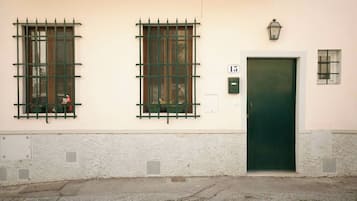 Un edificio con dos ventanas de celosía metálica, una puerta verde y un ventanal con una reja de metal.