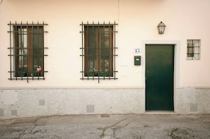Un edificio con dos ventanas de celosía metálica, una puerta verde y un ventanal con una reja de metal.