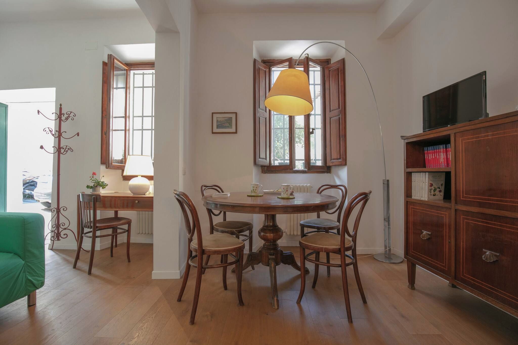 Un comedor con una mesa redonda de madera, cuatro sillas, una lámpara y una estantería.