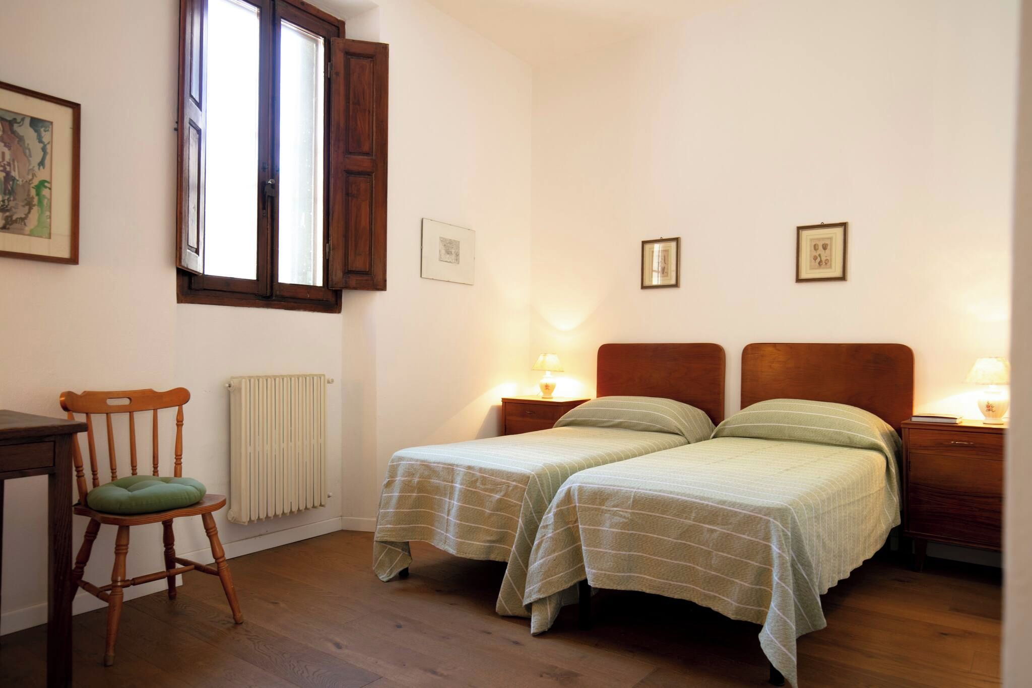 Un dormitorio con dos camas individuales, una silla de madera, un escritorio y un radiador.