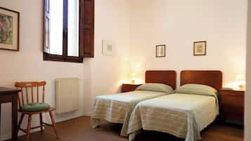 Un dormitorio con dos camas individuales, una silla de madera, un escritorio y un radiador.