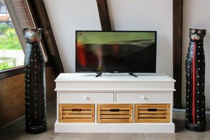 A white entertainment unit with a flat-screen TV, wooden drawers, and two decorative cat figures. - Holiday home with 1 bedroom (Hollern-Twielenfleth)