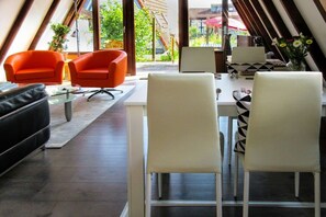 A modern interior with a dining area featuring a white table, black and white patterned chairs, and orange armchairs. - Holiday home with 1 bedroom (Hollern-Twielenfleth)