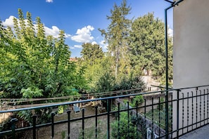 A balcony with a view of a garden, a stone wall, and a metal railing. - Aleardi (Florence)