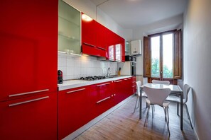 A modern kitchen with red cabinets, a gas stove, and a dining area with white chairs. - Aleardi (Florence)