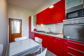 A kitchen with red cabinets, a white countertop, a stove, a sink, and a microwave. - Aleardi (Florence)