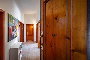A hallway with wooden doors, a white wall with a painting, and a white console table. - Aleardi (Florence)
