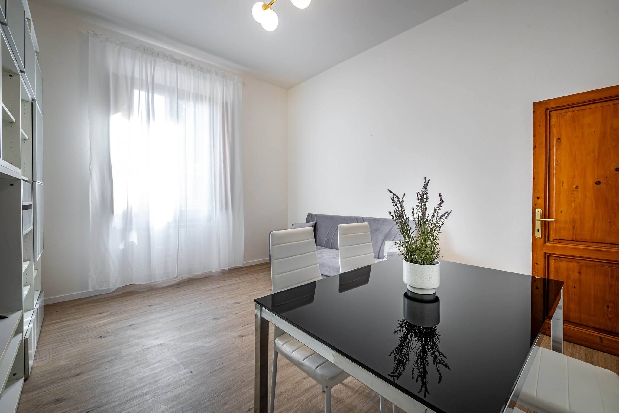 A modern living room with a black dining table, white chairs, a grey sofa, and a wooden door.