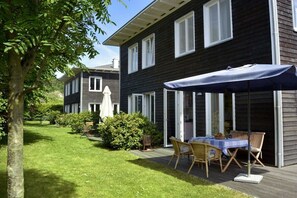 Ein zweistöckiges Haus mit überdachter Terrasse, Rasenfläche und Baum.