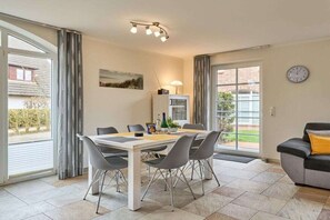 Ein modernes Wohnzimmer mit Essbereich, großen Fenstern, einer Couch und einer Wanduhr.