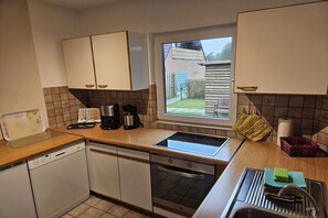 A compact kitchen with a dishwasher, oven, and a window with a view of a house. - North Sea holiday Stormhus (Sankt Peter-Ording)