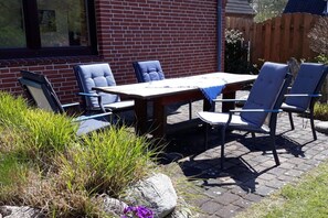 Eine Terrasse im Freien mit Tisch und Stühlen, umgeben von einer Ziegelmauer und einem Holenzaun.