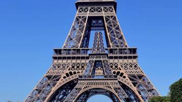 The Eiffel Tower with its intricate iron lattice structure, surrounded by a grassy area and a clear blue sky.