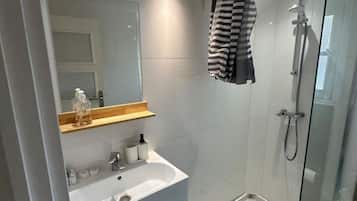 Ein modernes Badezimmer mit Duschkabine aus Glas, einem weißen Waschbecken und einem Holzlagerfläschchen.