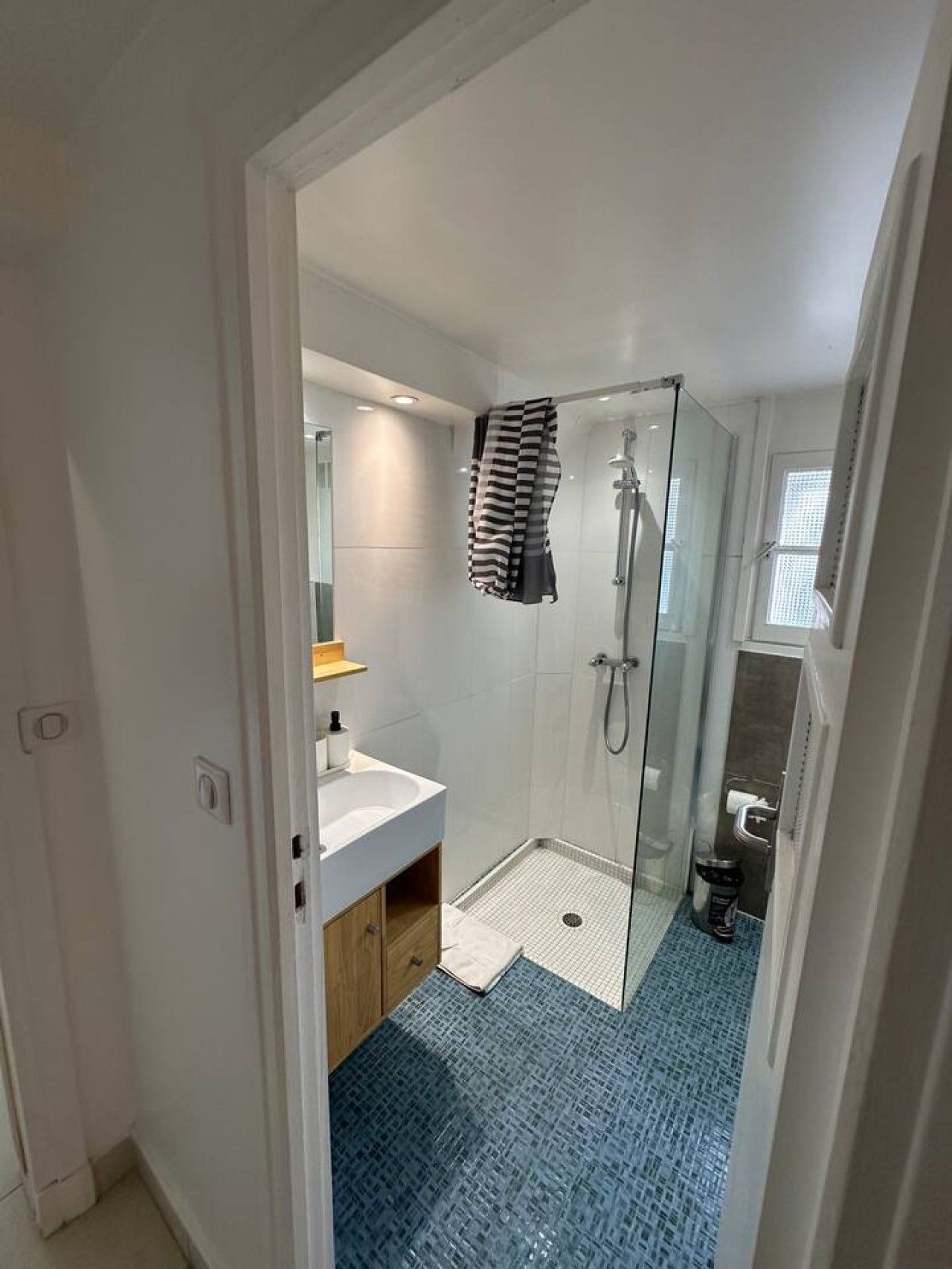 Un bagno moderno con cabina doccia in vetro, lavandino bianco e pavimento a motivi blu.