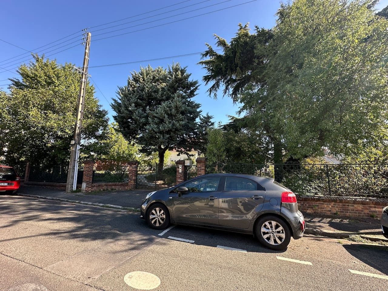 Un'auto parcheggiata in un parcheggio, sullo sfondo alberi e un muro in mattoni.
