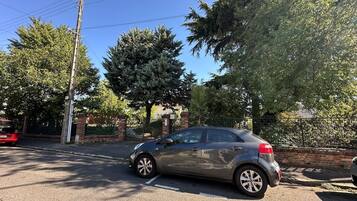 Un coche estacionado en un aparcamiento, con árboles y un muro de ladrillo al fondo.