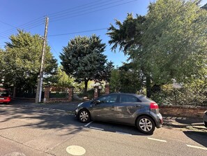 Un'auto parcheggiata in un parcheggio, sullo sfondo alberi e un muro in mattoni.