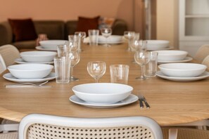 A dining table set with white plates, clear glasses, and cutlery, surrounded by chairs. - 20 min from Paris - 2 parking spaces - 6 beds - 3 bedrooms - 2 bathrooms (Argenteuil)