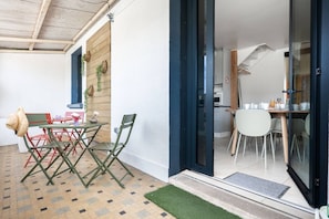 A dining area with a table and chairs, a kitchen visible through glass doors, and a small outdoor seating area with a hat on a chair. - Spacious Apartment—5 Bedrooms—Accommodates 10 Guests—20 Minutes from Paris—2 Parking Spaces (Argenteuil)