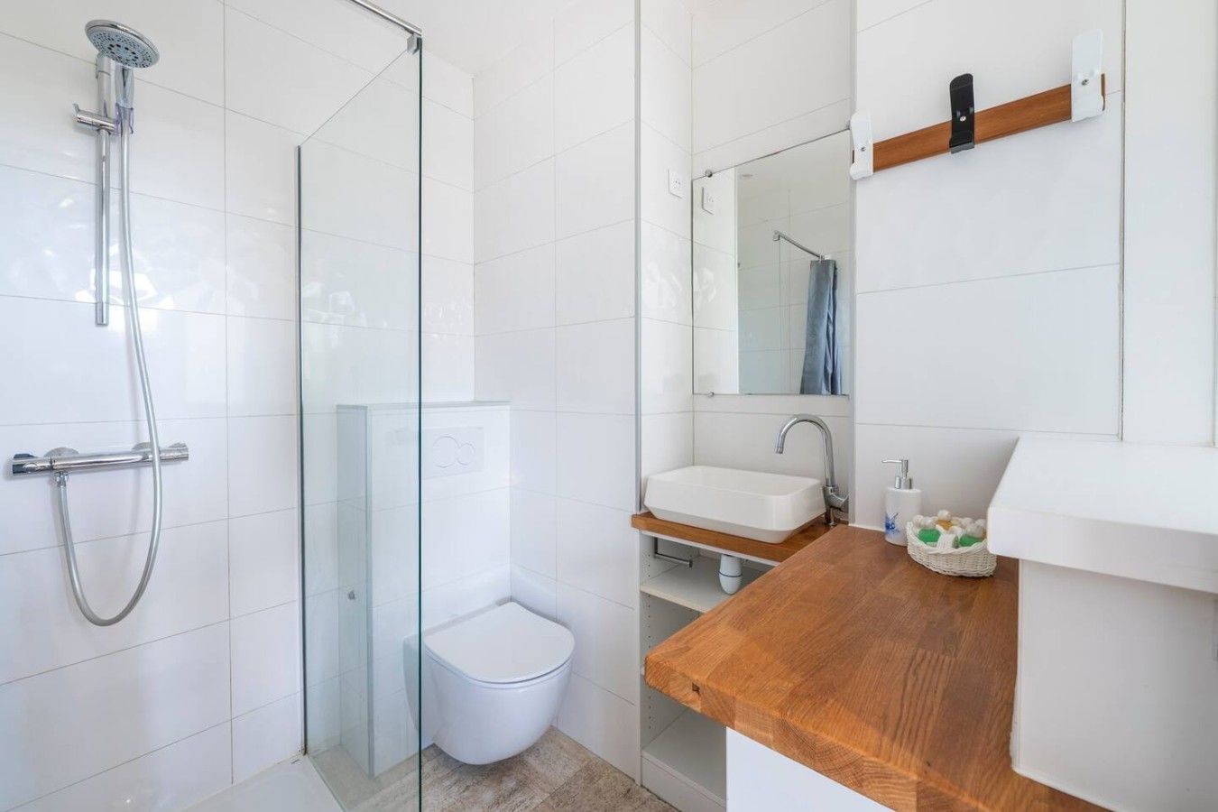Une salle de bain moderne avec une douche à parois de verre, des toilettes blanches, un meuble-lavabo en bois et un miroir.