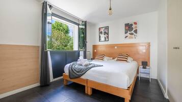 Une chambre à coucher moderne avec un grand lit, une fenêtre avec des rideaux, une table de chevet et des œuvres d’art accrochées au mur.