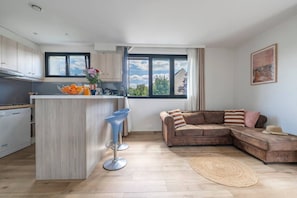 Eine moderne Küche mit Kochinsel, Barhocker, einer Couch und einem großen Fenster mit Ausblick.