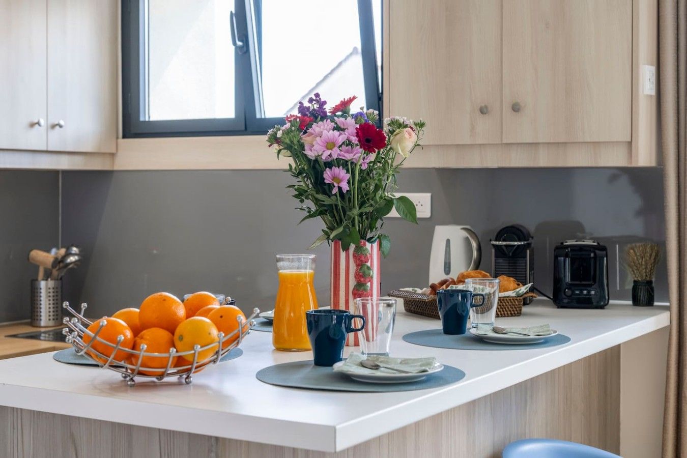 Eine Küchenarbeitsplatte mit Obstschale, Saftkaraffe, Blumen in einer Vase, Kaffeemaschine und Toaster.