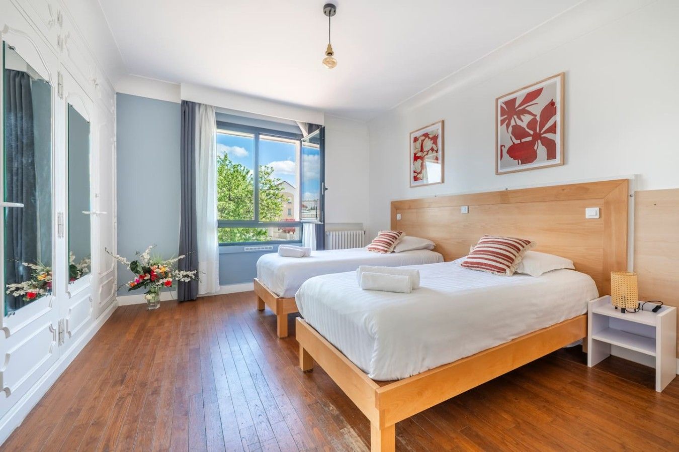 A hotel room with two beds, a large window, and a view of greenery.