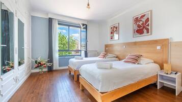 A hotel room with two beds, a large window, and a view of greenery.