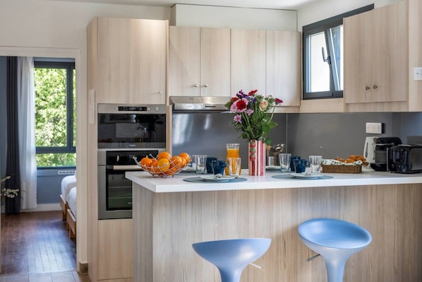 Eine moderne Küche mit Holzschränken, einer zentralen Kochinsel mit Barhocker und einem Essbereich mit Frühstücksbereitstellung, darunter Obst, eine Blumenvase und ein Toaster.