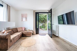 A modern living room with a sectional sofa, a flat-screen TV, and a view of a garden through an open door.