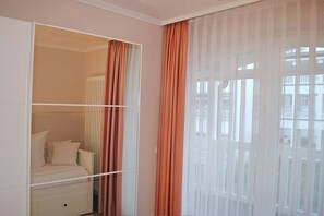 Ein Schlafzimmer mit einem Bett, einem Kleiderschrank und einem Fenster mit transparenten Vorhängen.