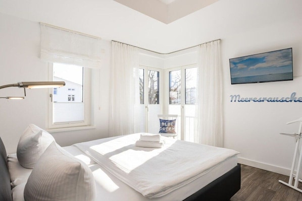 A hotel room with a bed, a desk, a chair, a window, a television, and a wall with a sign. - No. 20 in Villa Poseidon (Ostseebad Binz)