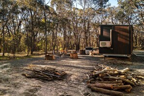 A campsite with a portable RV, firewood, and a wooded area.