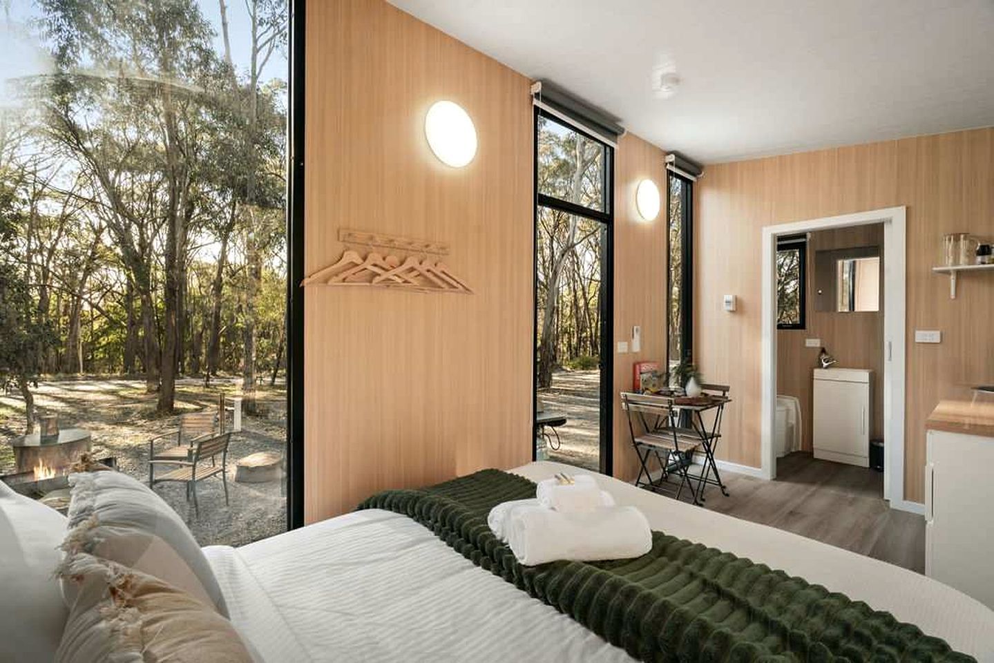 A modern bedroom with a large bed, a wooden wall, and a view of the outdoors.
