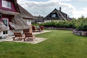 A traditional thatched-roof house with a lawn and outdoor seating area.