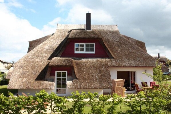 A thatched-roof house with a red door and white window frames.